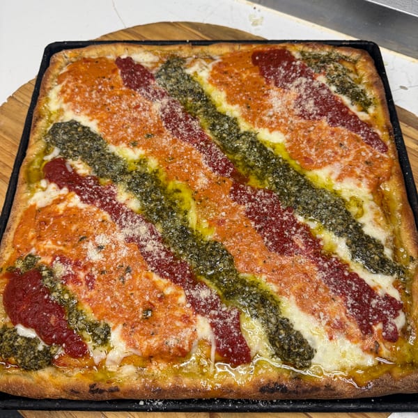 A rectangular pizza with diagonal stripes of red sauce, pesto, and cheese, sprinkled with parmesan.