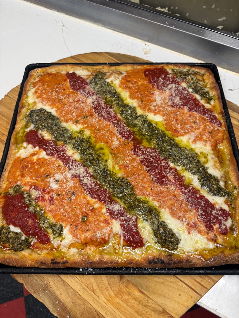 A rectangular pizza with diagonal stripes of red sauce, pesto, and cheese, sprinkled with parmesan.
