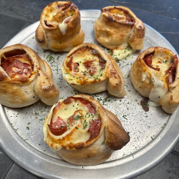 Six golden-brown pizza rolls with melted cheese and pepperoni on a silver pizza pan.