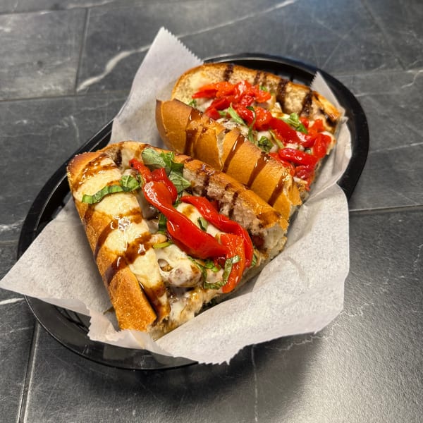 Two halves of a sub sandwich with melted cheese, red peppers, and basil, drizzled with sauce.