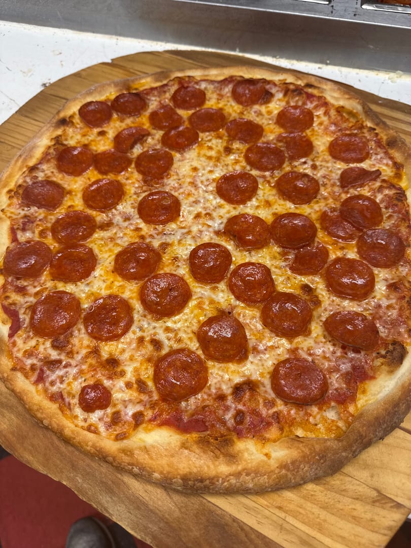 A freshly baked pepperoni pizza with melted cheese and a golden crust on a wooden peel.